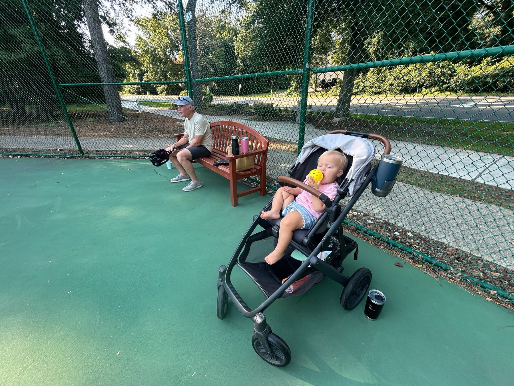 Dad on the bench, niece chewing a pickleball